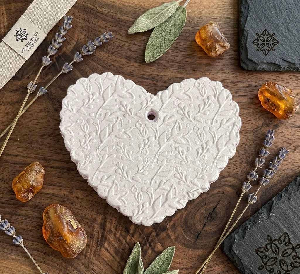 Heart-shaped white ceramic ornament on a wooden surface with lavender and amber stones.