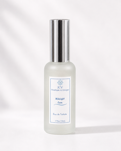 A frosted glass perfume bottle with a shiny silver cap, featuring a white label with blue text that reads 'JCV Boutique & Design Midnight Cavi Eau de Toilette'. The bottle is centered against a clean white background with soft, artistic leaf shadows.