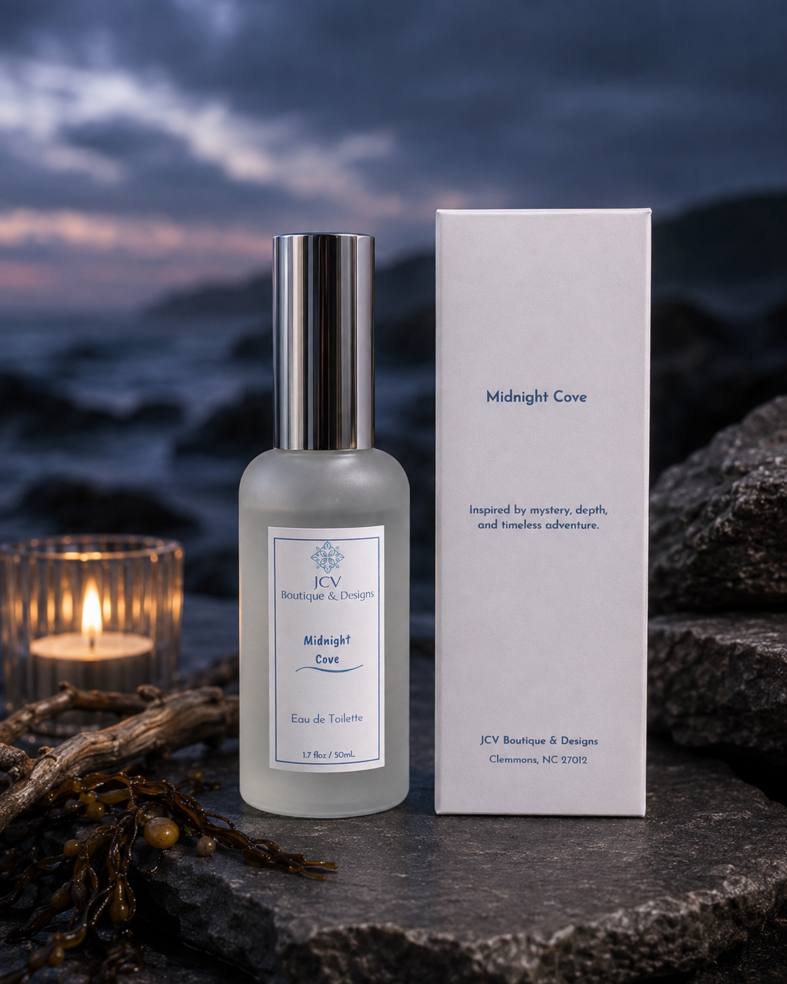 A frosted glass bottle of JCV Bougie & George Midnight Cove Eau de Toilette stands next to its white cardboard box, styled on a dark rocky surface with a lit candle and driftwood in the foreground against a moody ocean sunset background.