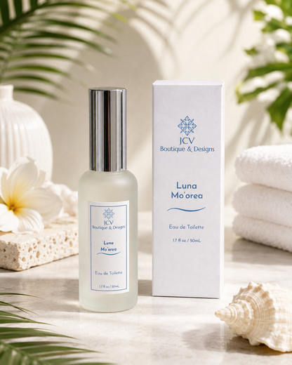 A bottle ofJCV Boutique & Designs Luna Mo'orea Eau de Toilette next to its white packaging box, styled with tropical leaves, a white flower, a sponge, and a seashell on a light stone surface.