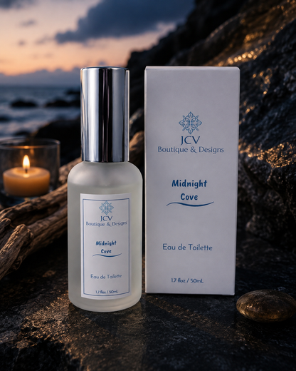 A bottle of JCV Boutique & Designs Midnight Cove Eau de Toilette stands next to its white packaging box on a dark rocky surface, with a lit candle and a sunset ocean scene in the background.