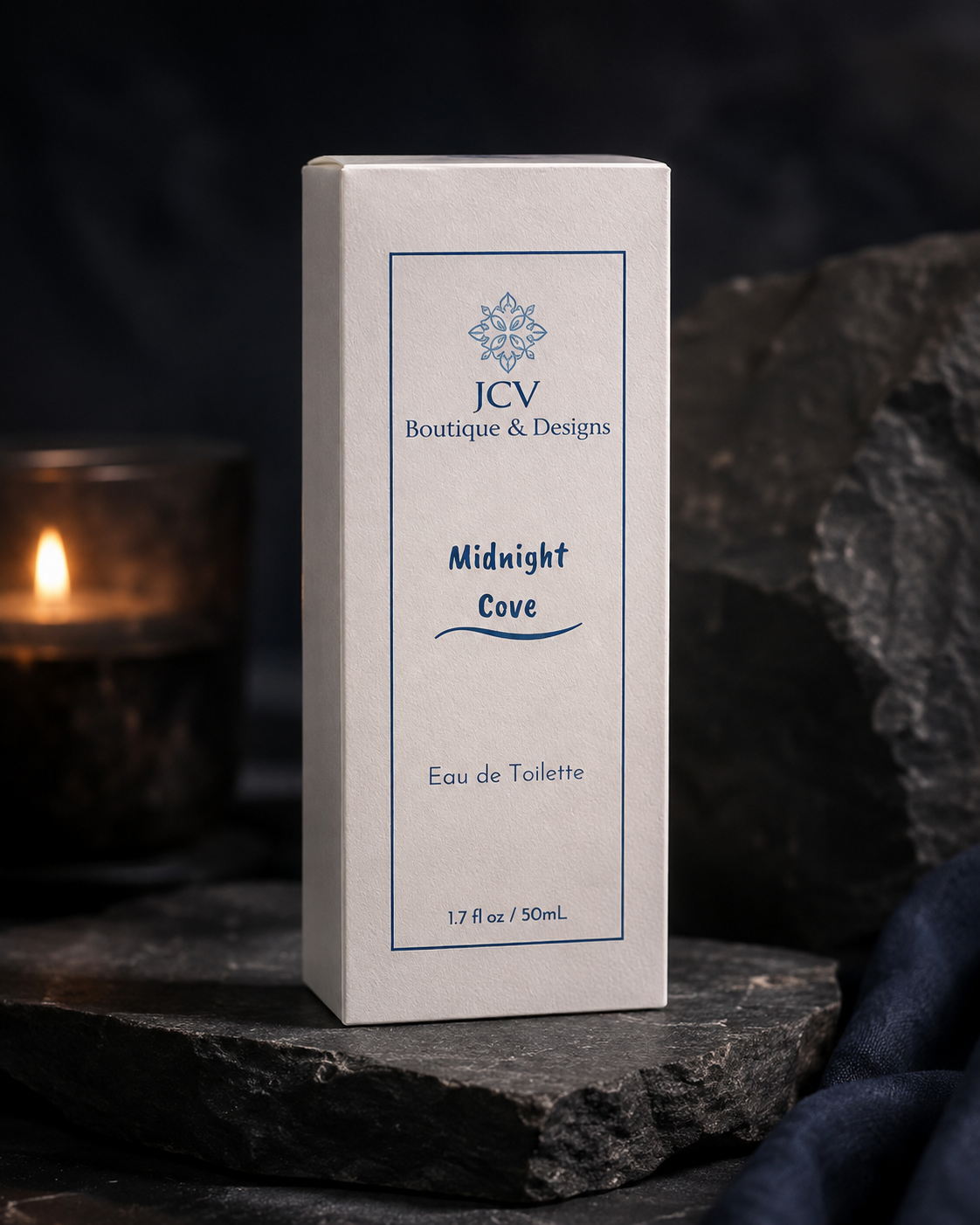 A rectangular product box for JCV Boutique & Designs 'Midnight Cove' Eau de Toilette, standing upright on dark slate with a blurred lit candle in the background.
