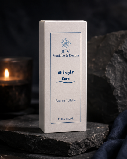 A rectangular product box for JCV Boutique & Designs 'Midnight Cove' Eau de Toilette, standing upright on dark slate with a blurred lit candle in the background.