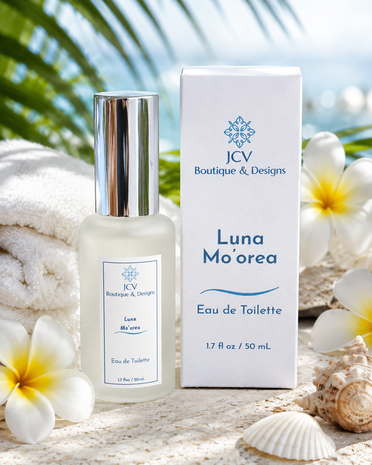 JCV Boutique & Designs Luna Mo'orea Eau de Toilette bottle and packaging box displayed on a sandy beach-style surface with tropical flowers, shells, and a towel in the background.