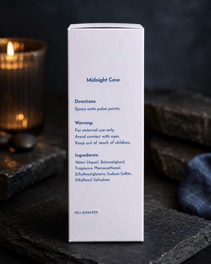 A tall white rectangular product box standing upright on a dark stone surface, with printed blue text reading 'Midnight Cove' and usage directions. A blurred lit candle and dark background are visible behind it.